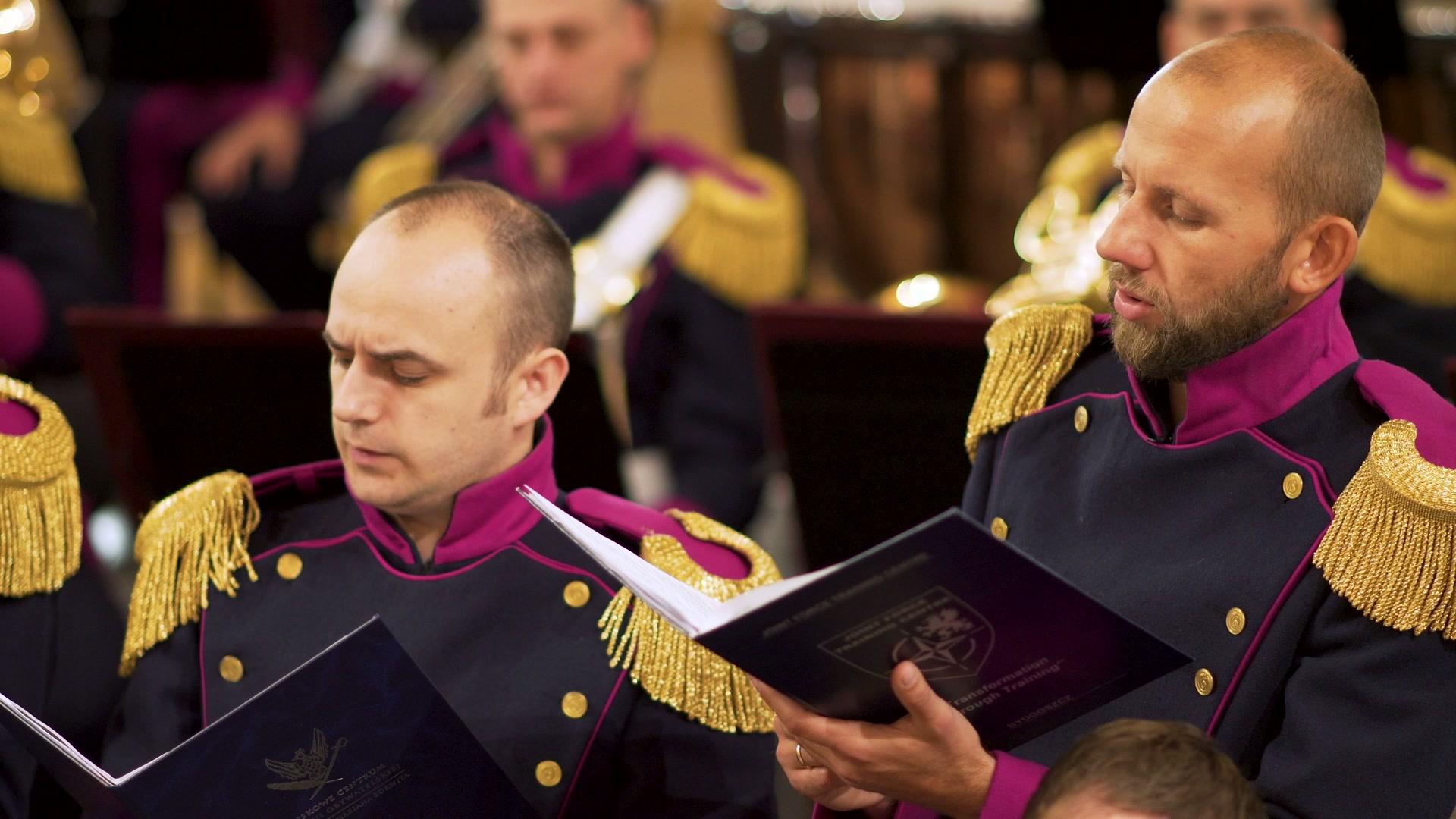 Muzycy orkiestry śledzą partytury w ciepłym świetle sceny podczas nagrania Missa Vaticana.