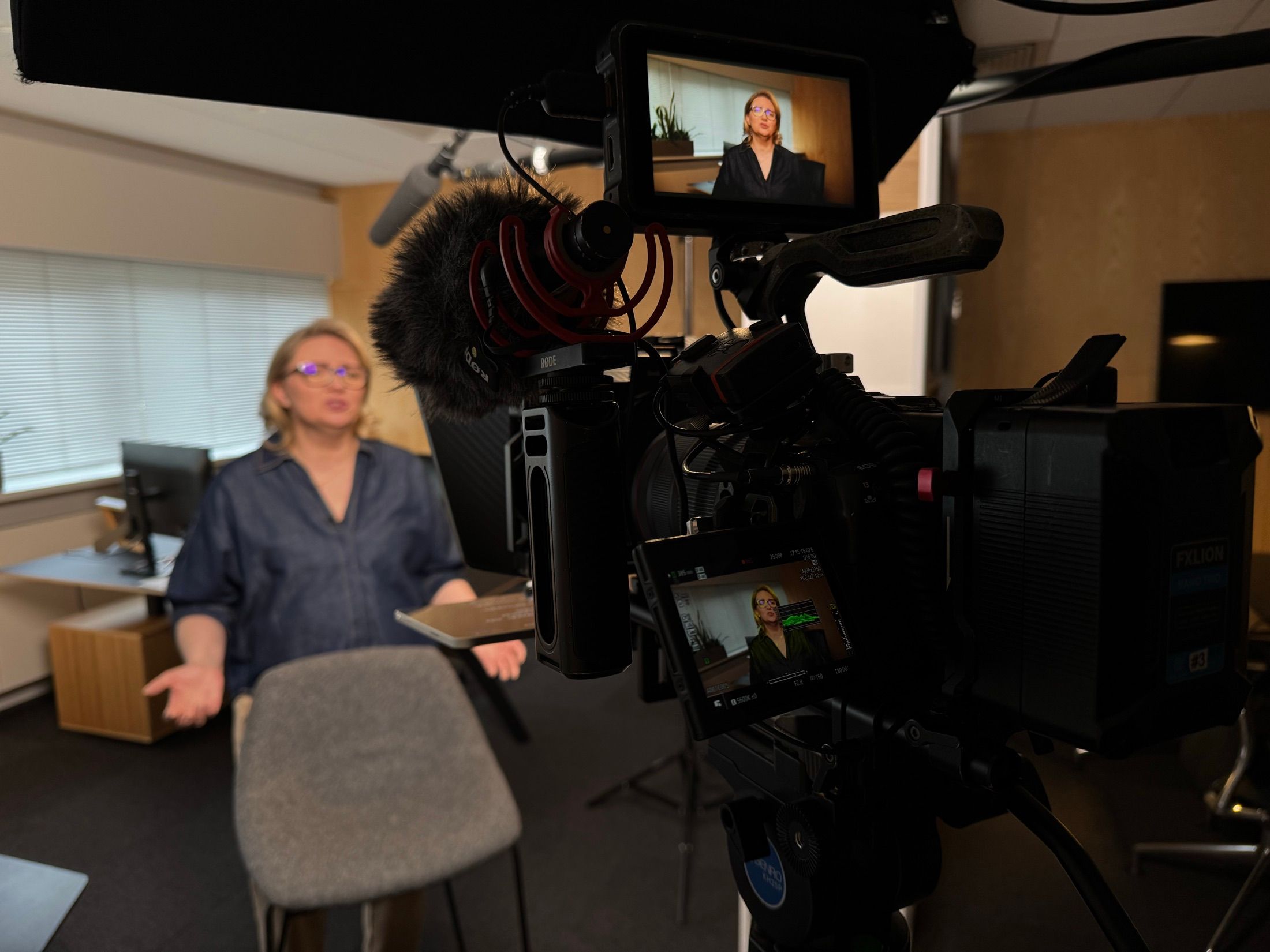 Hinter der Kamera bei einem Büro-Interview, zwei Monitore zeigen eine sprechende Frau.