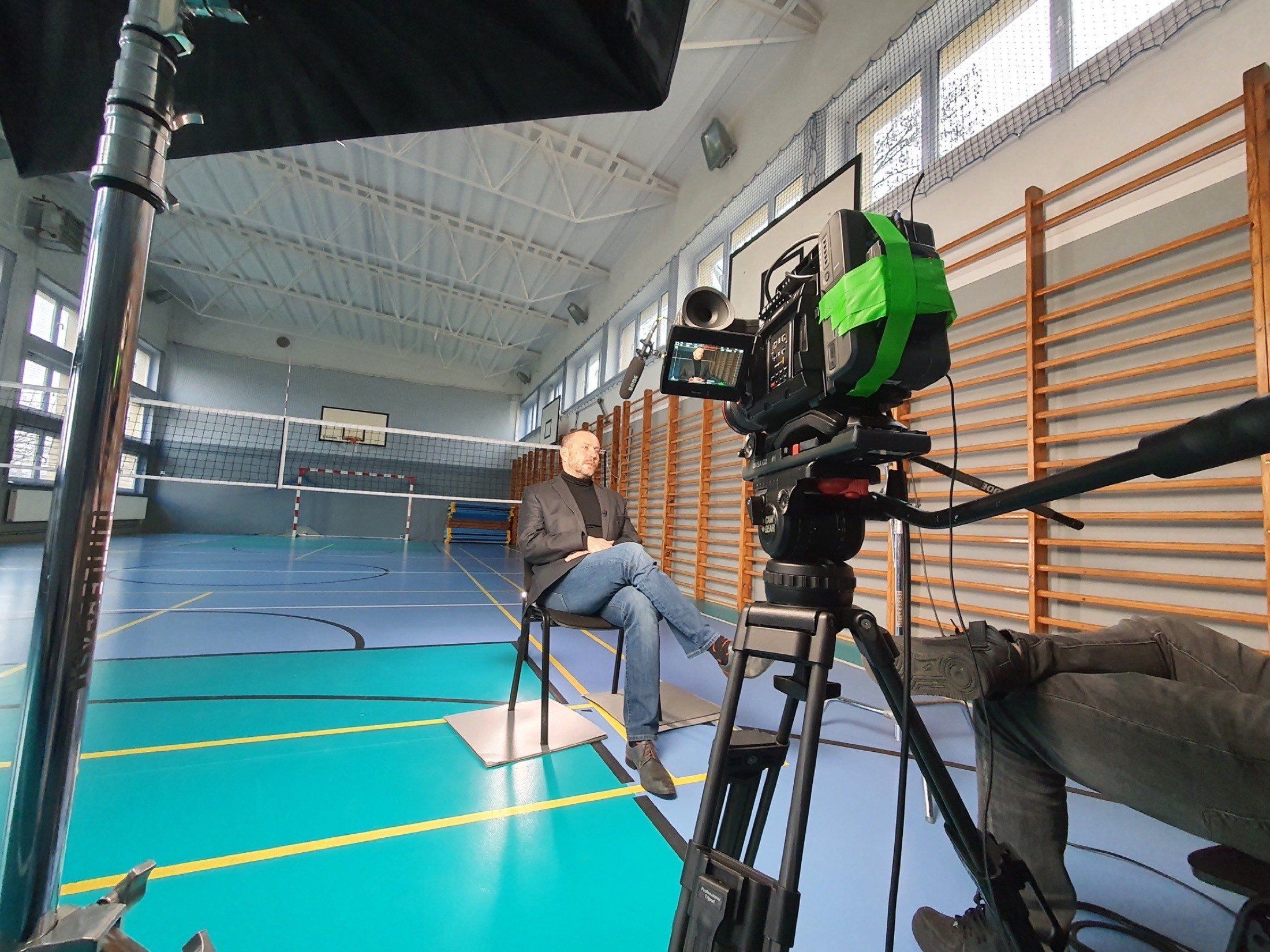 Ein Interview in einer Sporthalle: die Person sitzt mittig auf dem Spielfeld, Kamera auf dem Stativ.