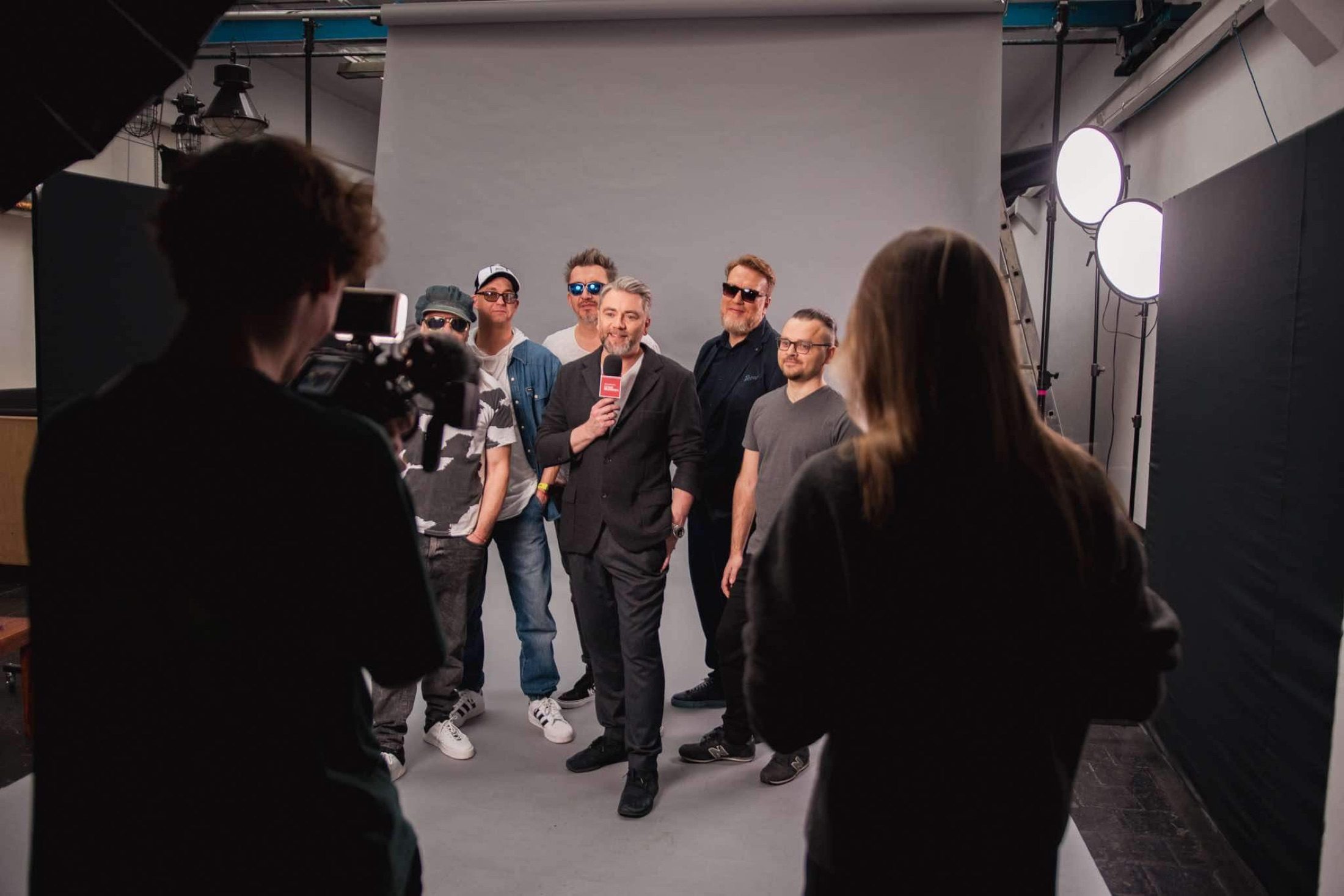 Oświetlone studio: grupa na jednolitym tle z prowadzącym, w pełnym świetle produkcyjnym.
