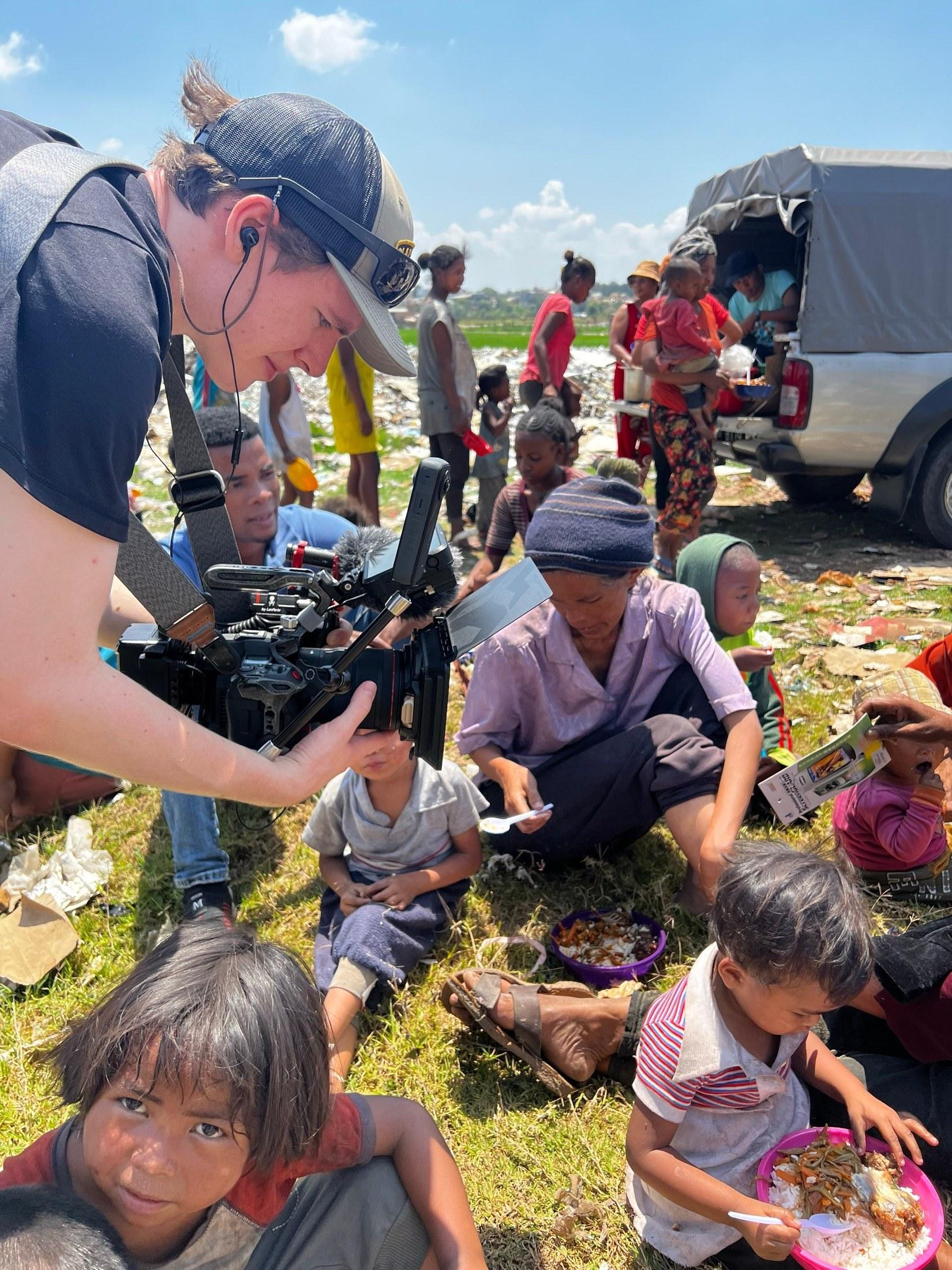 Ein Kameramann filmt einheimische Kinder, die neben einem Lastwagen essen, an einem Drehort in Madagaskar.